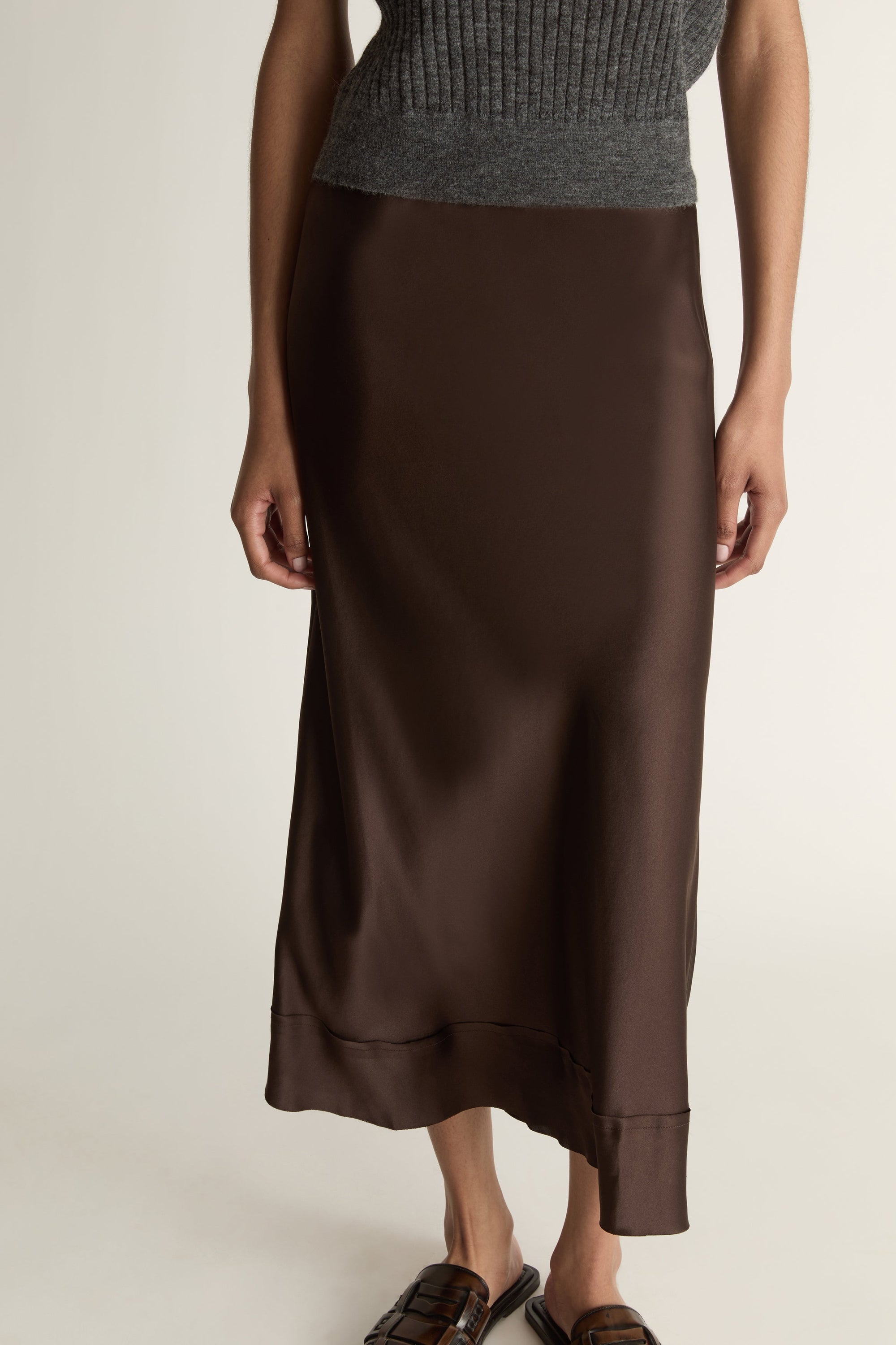 Woman wearing a sleeveless gray top and brown skirt on a plain background