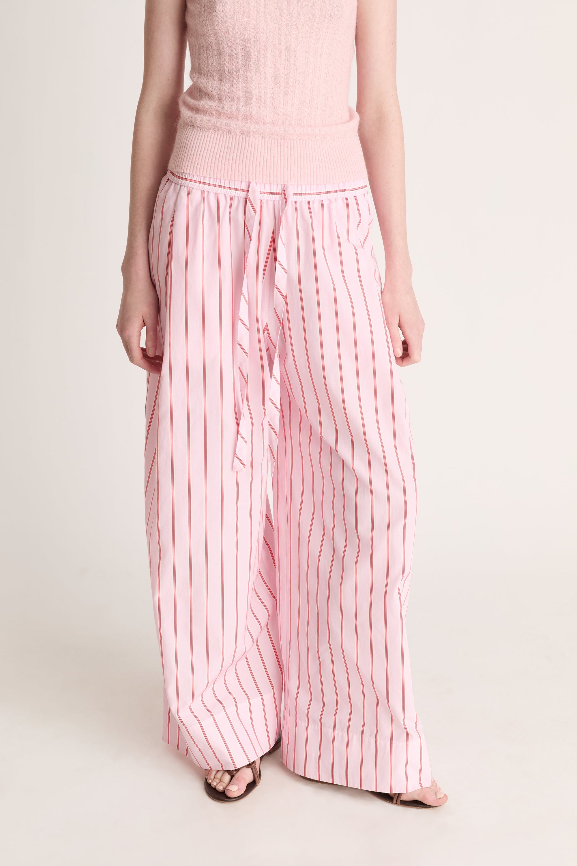 Close up of a woman wearing pink knit top with pink striped pants on a white background