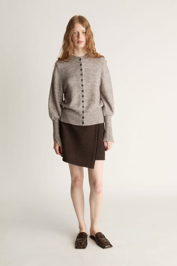 Woman wearing a gray sweater and brown skirt on a plain background