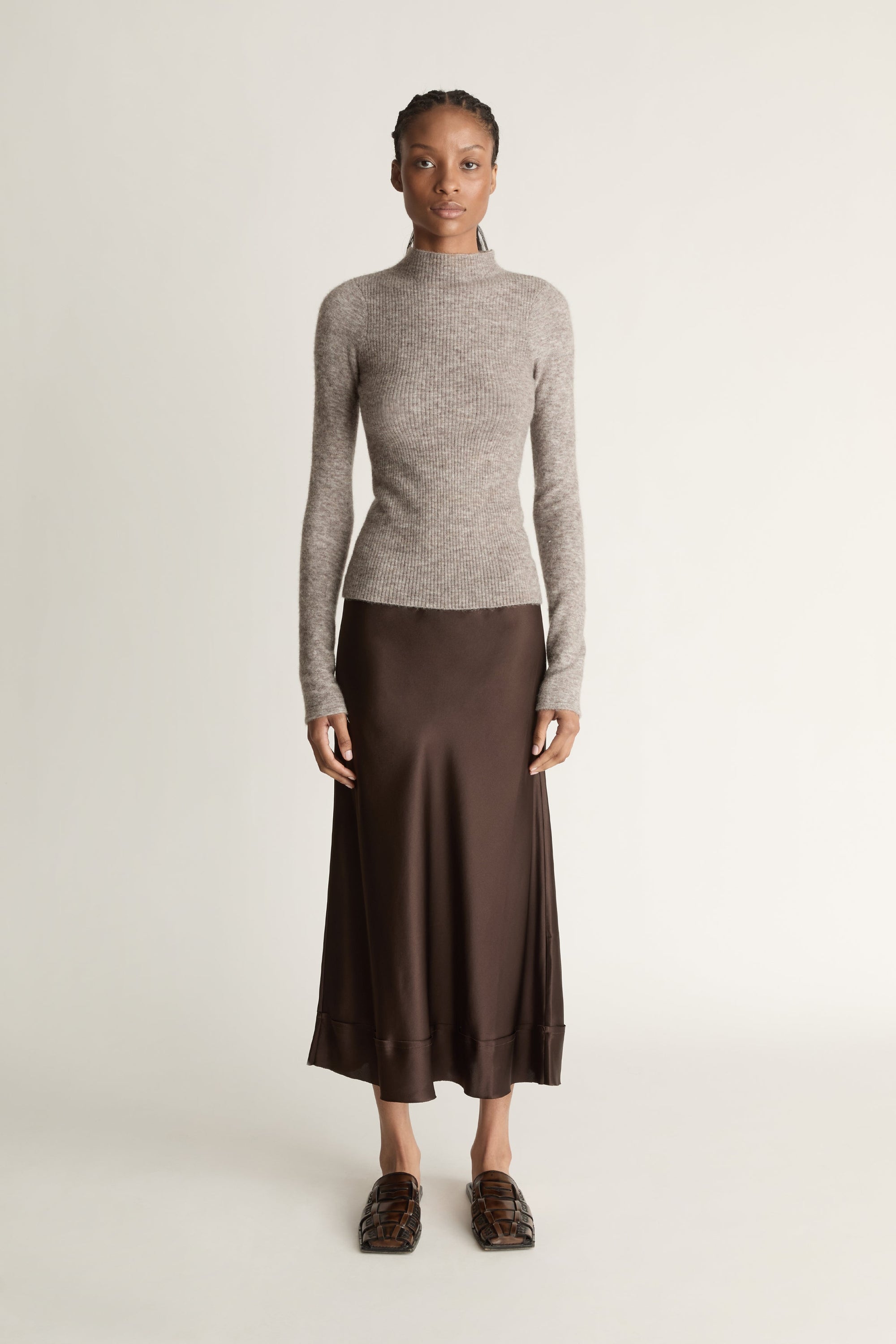 Woman wearing a gray turtleneck sweater and brown skirt against a beige background