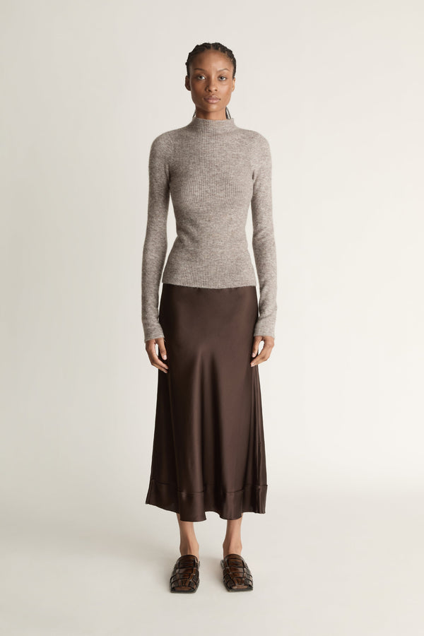 Woman wearing a gray turtleneck sweater and brown skirt against a beige background