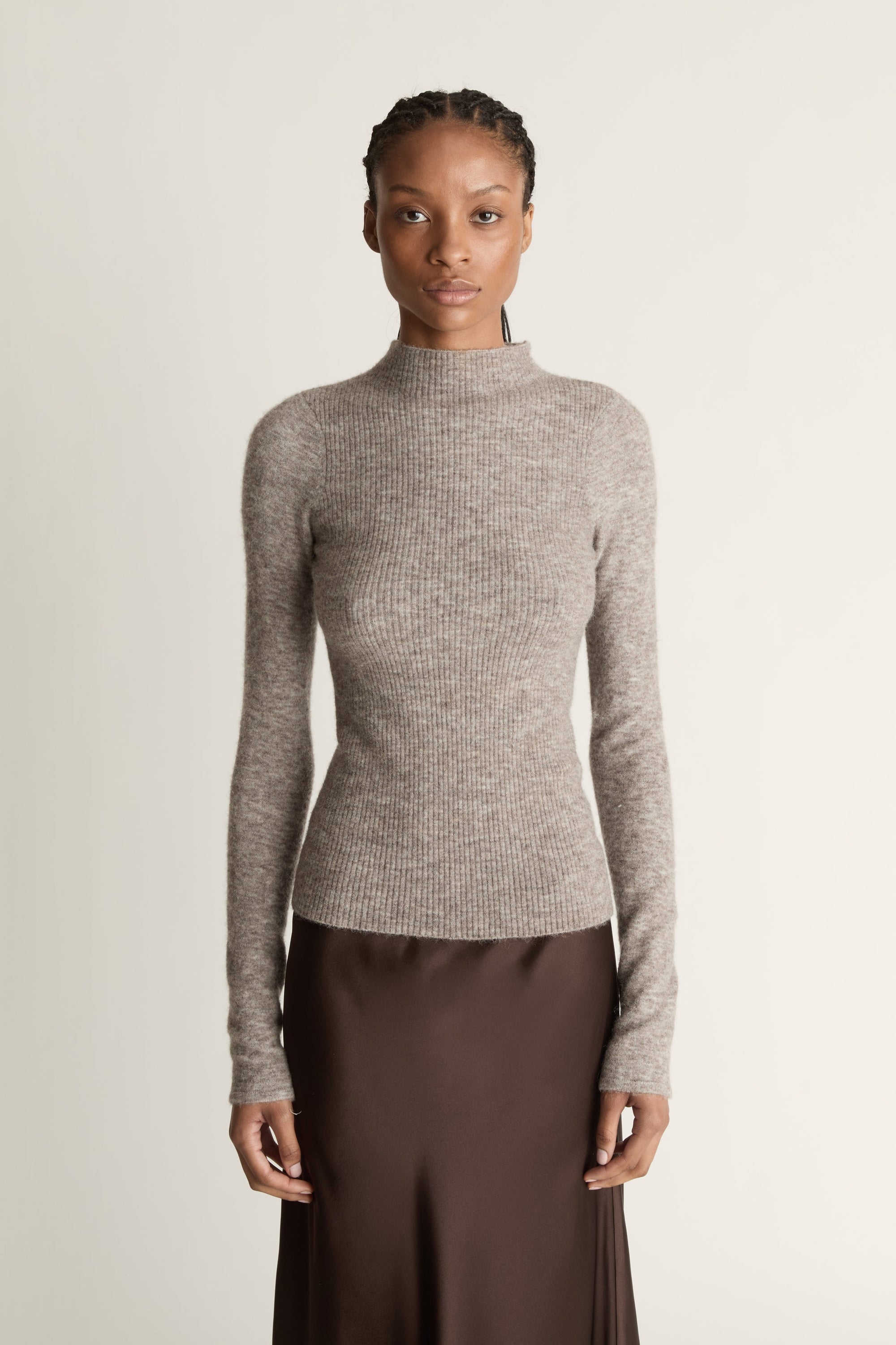 Woman wearing a gray turtleneck sweater and brown skirt against a beige background