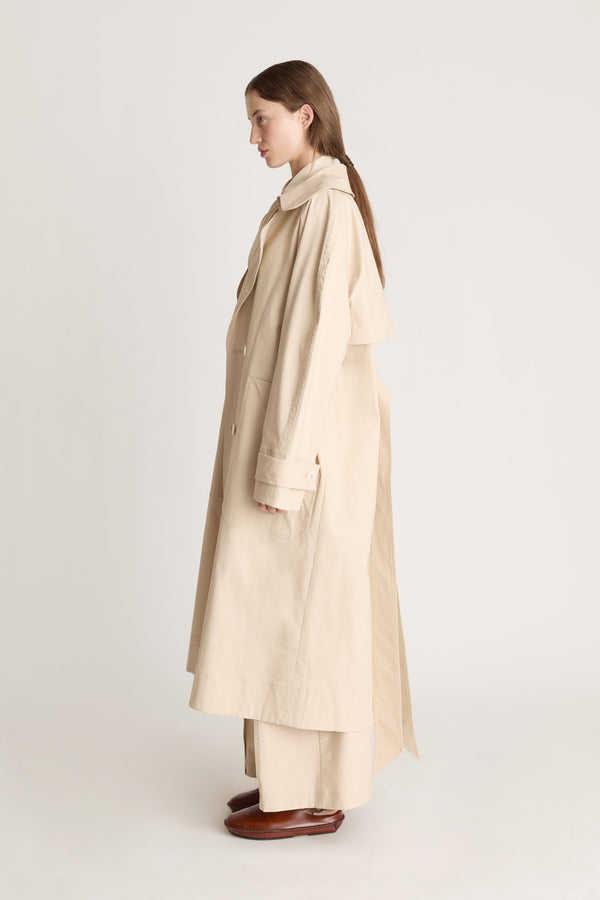 Woman wearing a beige trench coat holding a black bag on a white background