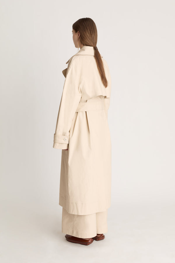 Woman wearing a beige trench coat holding a black bag on a white background