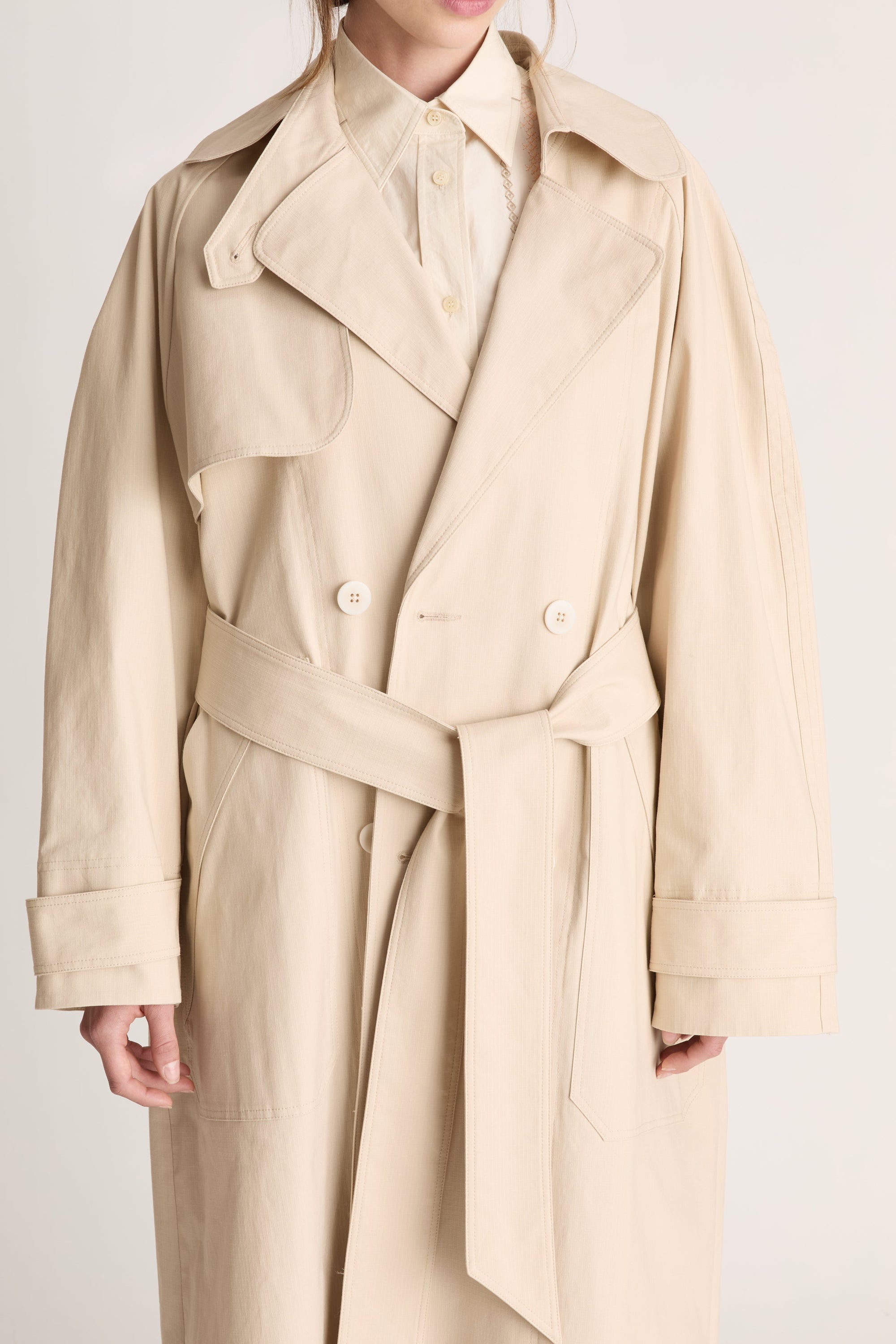 Beige trench coat worn by a person on a white background