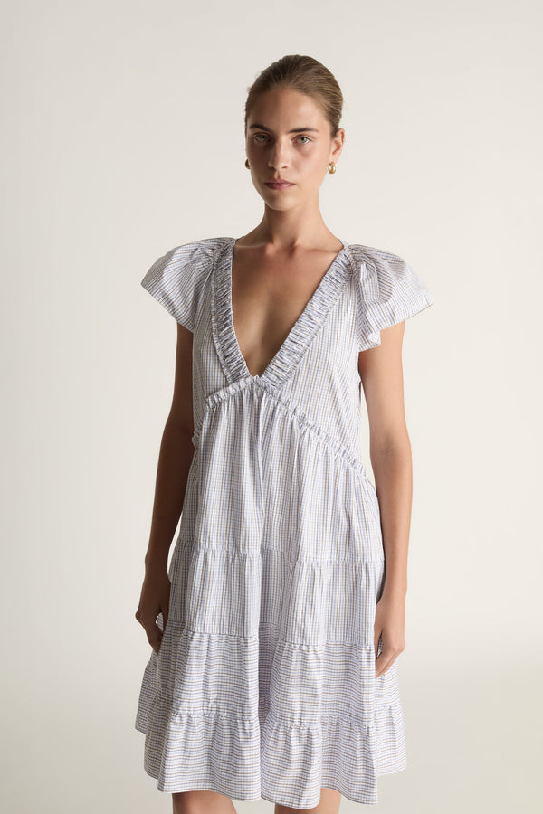 Woman wearing a blue printed dress with ruffled sleeves on a plain background