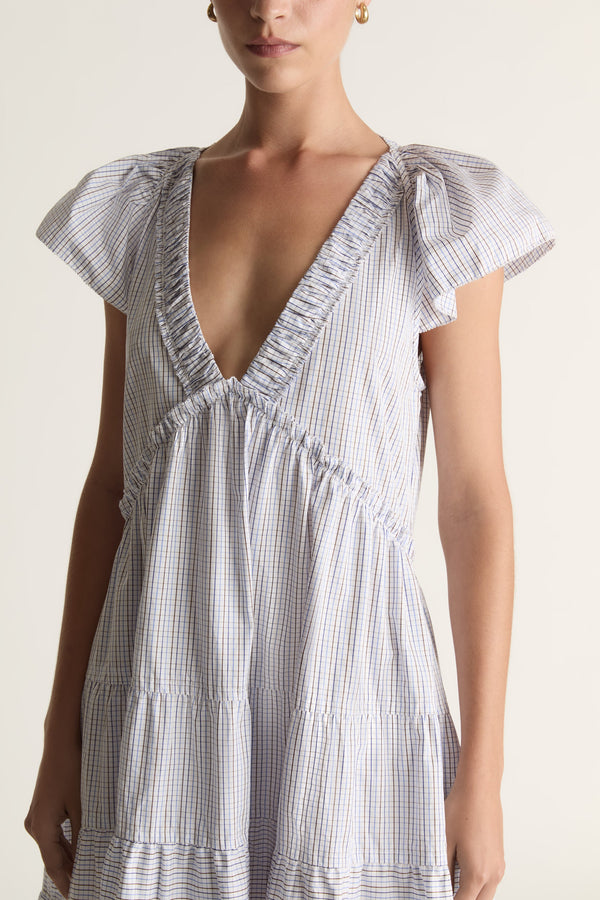 Woman wearing a blue printed dress with ruffled sleeves on a plain background